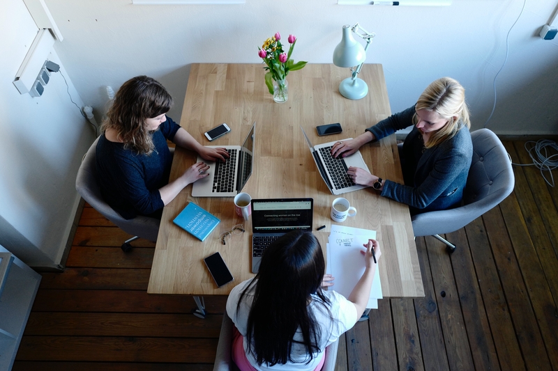 Tre kvinder sidder omkring et bord og arbejder på hver sin computer