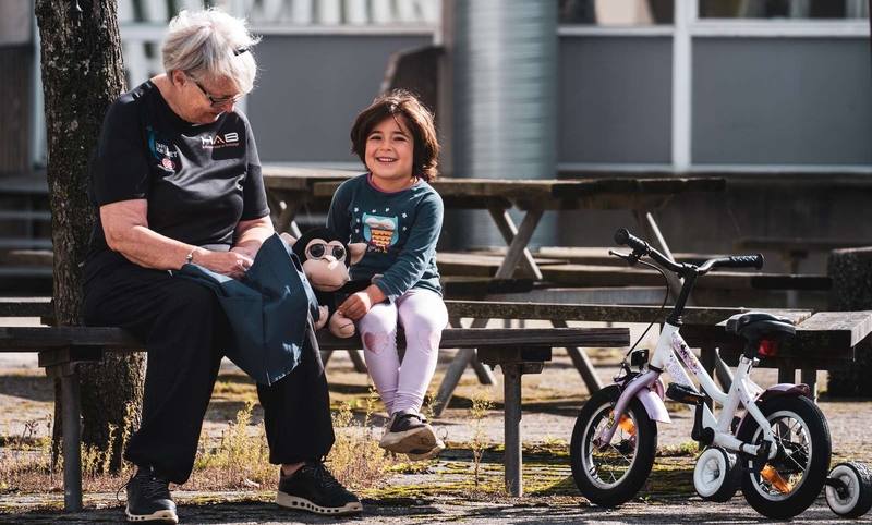 Old woman sitting on bench next to a young girl.