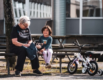 Old woman sitting on bench next to a young girl.
